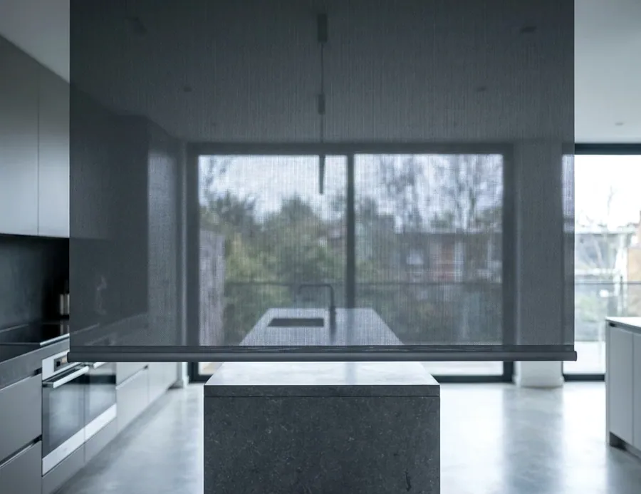Sunscreen roller blind filtering midday light over glass doors, garden visible through the open weave