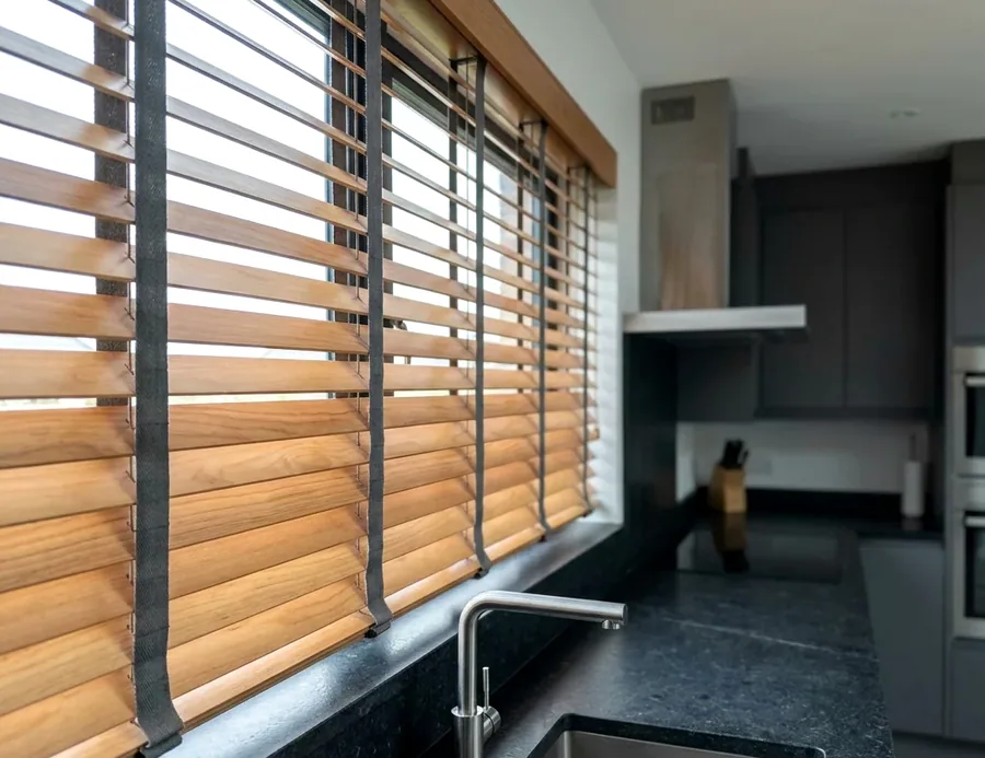 Timber venetian blind slats tilted open above a kitchen counter, warm light between the slats